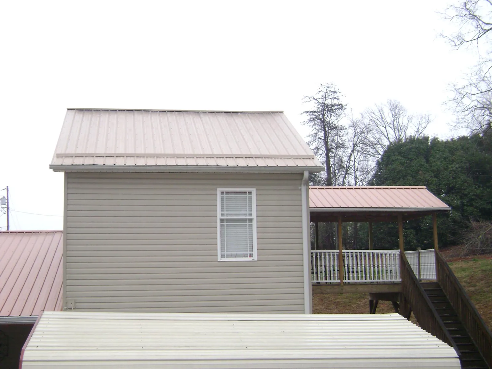 Tan metal roofs on a two story addition and attached porch, from a Roof Replacement job in Wendell